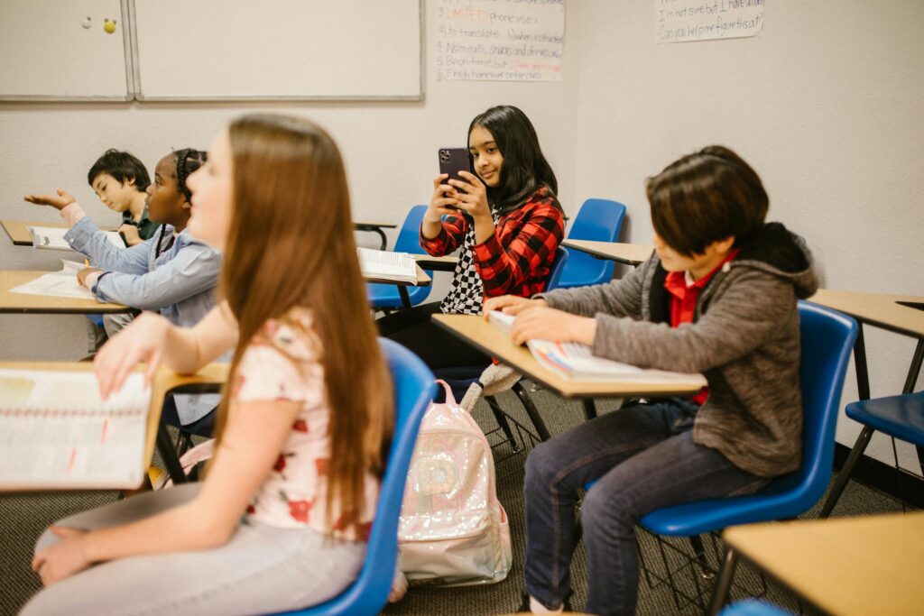 Students in a classroom setting with a girl taking a photo using a smartphone.